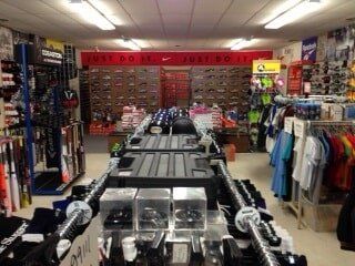 Interior of H Mickel Sports store, showing racks of clothing, uniforms, and sports equipment.